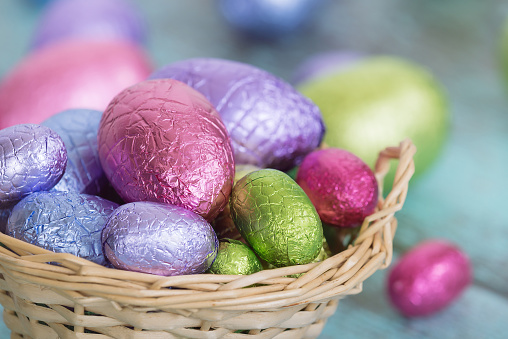 Pastel color Easter chocolate eggs in a basket, closeup with shallow depth of field