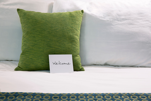 Welcoming hotel bed with pillows and welcome card close up.