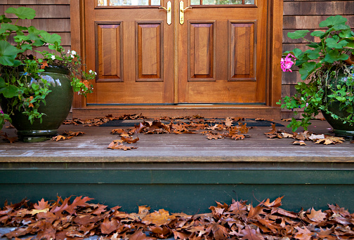 Autumn leafs on the front porch with wooden french door in the background and two flower pots on each side