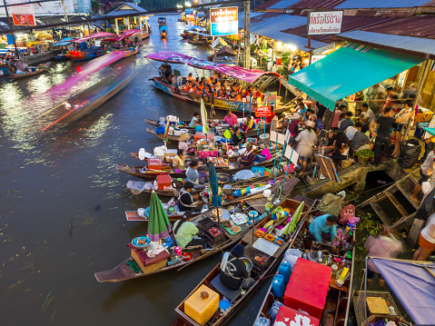 Samut Songkhram, Thailand - July 20, 2013: Boats lined along the river in Amphawa Floating Market as vendors and shop owners get busy with customers.