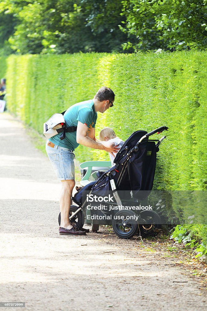 Father and son in baby buggy Düsseldorf, Germany - June 8, 2014: Capture of adult man taking little boy out of baby buggy. Behind them is a bench. Scene is in park of Schloss Benrath in Düsseldorf. At right side are woods and hedge. Summer shot. Adult Stock Photo