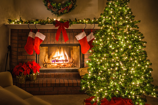 Christmas tree and decorations around the warmth of the blazing fire in the fireplace. Christmas tree, Christmas fireplace, stockings, lights, ornaments, poinsettias, bow.