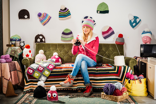 Young woman knitter portrait on couch with winter hats