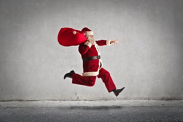 Old man dressed as santa claus jumping high in the air with his bag on his shoulder