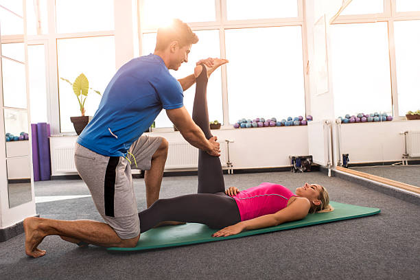 istock Smiling coach assisting young woman in doing stretching exercises. 497407272