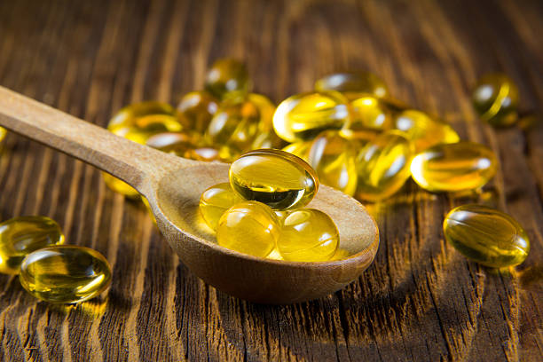 Cod-liver oil, omega3, vitamin D Cod-liver oil, omega3, vitamin D capsules on wooden spoon animal internal organ stock pictures, royalty-free photos & images
