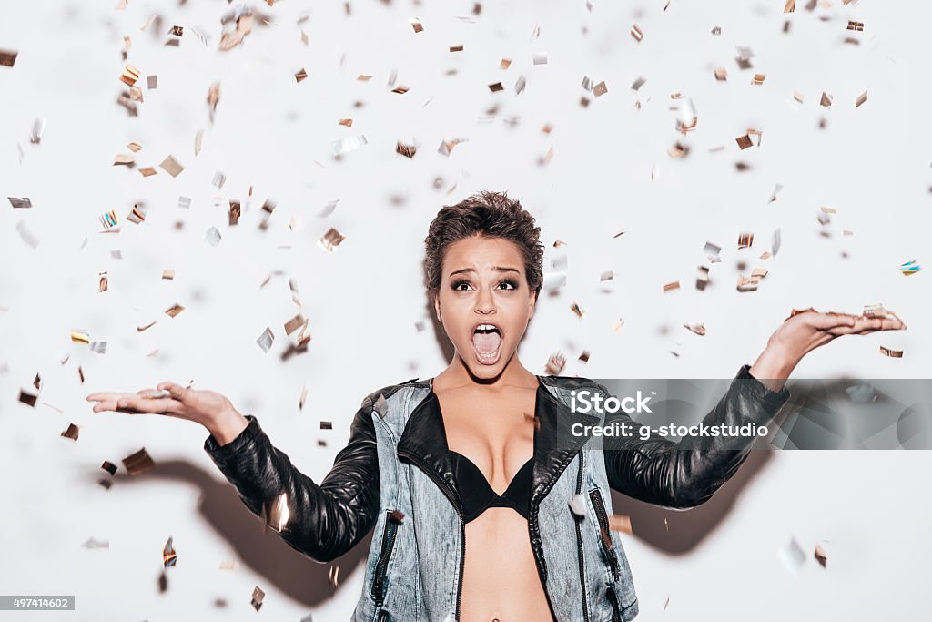 Confetti fun. Beautiful young short hair woman in black underwear and leather jacket throwing confetti while standing against white background 2015 Stock Photo