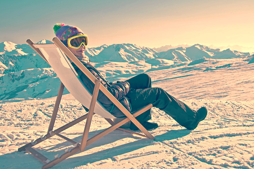 Girl sunbathing in a deckchair on the side of a ski slope, vintage process