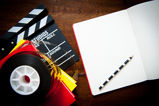 Screenwriter desktop detail with clapper, film reel notebook and pencil