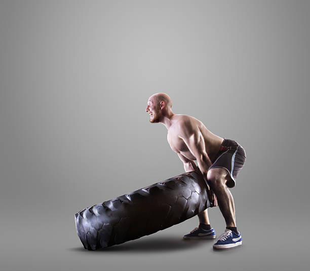 istock Athletic young man lifting a tire on gray studio background 497419188