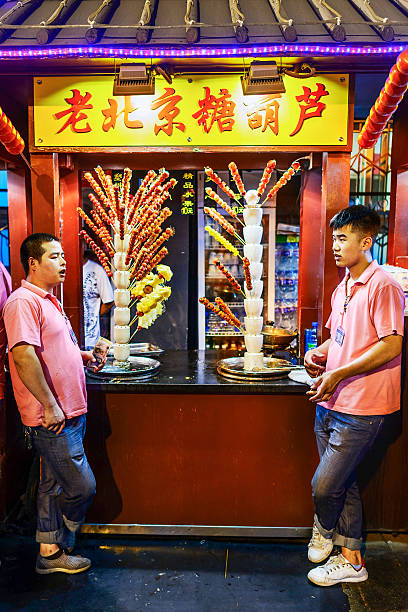 Ancient Beijing Style Street Beijing, China -  August 18, 2015: Seller selling Ancient Beijing Tomatoes on sticks. Ancient Beijing Style Street at night. Located in Wangfujing Snack Street. Beijing, China. wangfujing stock pictures, royalty-free photos & images
