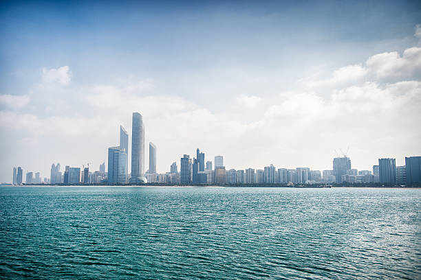 Water level view of skyscrapers in Corniche bay in Abu Dhabi, UAE. Waves of turquoise water are in front view and blue sky combined with building exterior is in the distance.