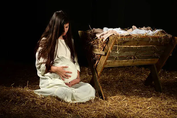 Pregnant Mary holding stomach at manger on Christmas Eve