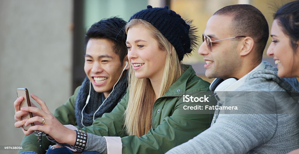 Taking a Cell Phone Selfie A multi-ethnic group of teenage friends are hanging out after school together taking a selfie with a cell phone. 2015 Stock Photo