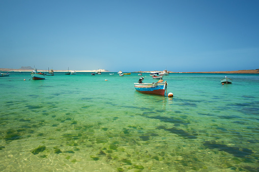 A sunny day on Boa Vista, one of the islands of Cape Verde which sit off the west coast of Africa. Brightly coloured fishing boats bob around in the clear waters of the harbour of Sal Rei, the principal settlement of Boa Vista.