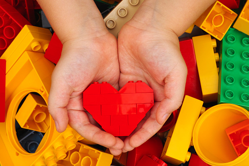 Tambov, Russian Federation - September 07, 2015: Lego red heart in child hands with Lego Duplo blocks background. Studio shot.