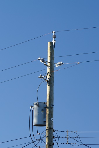 A residential utility pole with a grey transformer set against a clear blue sky.