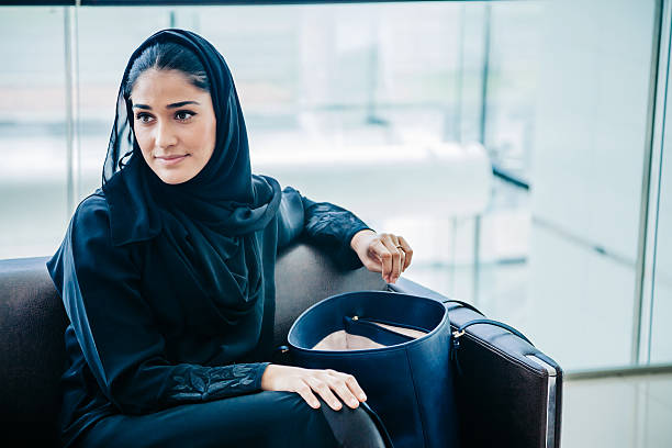 Beautiful Emirati woman at lounge Portrait of beautiful young arabic woman with traditional black scarf abaya clothes sitting at waiting lounge room at modern shopping mall in Dubai, UAE arab woman stock pictures, royalty-free photos & images
