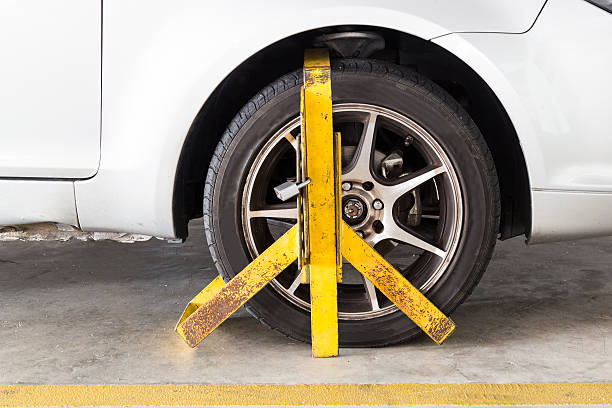 Car wheel clamped for illegal parking violation at car park Front car wheel clamped for illegal parking, a violation at commercial car parks car boot stock pictures, royalty-free photos & images