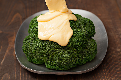 A high angle close up horizontal photograph of golden cheese sauce flowing unto lightly steamed broccoli.