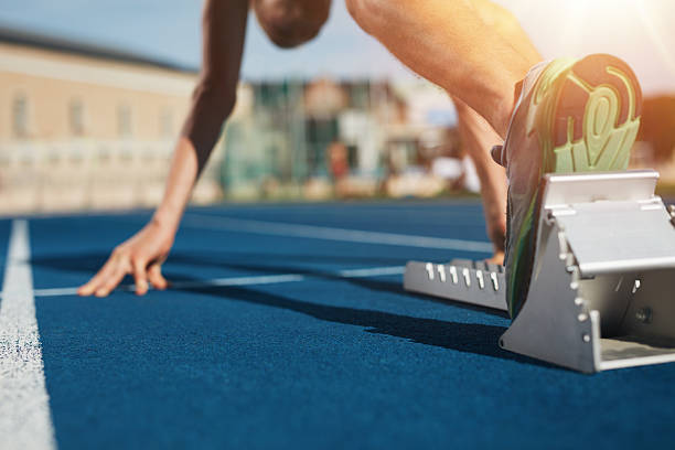 Sprint start on race track Feet on starting block ready for a spring start.  Focus on leg of a athlete about to start a race in stadium with sun flare. sprint stock pictures, royalty-free photos & images