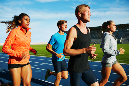 Group of multiracial professional athletes practicing running in stadium. Male and female athletes running together on racetrack.