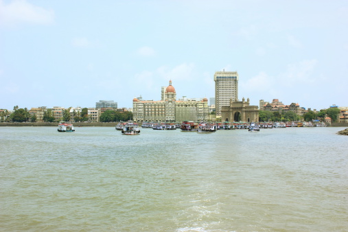 Panorama of Mumbai. Hotel 'Taj' and monument The Gateway of India. Located on the waterfront in Apollo Bunder area in South Mumbai, The Gateway of India was built to commemorate the visit of King George V and Queen Mary to Bombay, prior to the Delhi Durbar, in December 1911. Its design is a combination of both Hindu and Muslim architectural styles, the arch is in Muslim style while the decorations are in Hindu style.