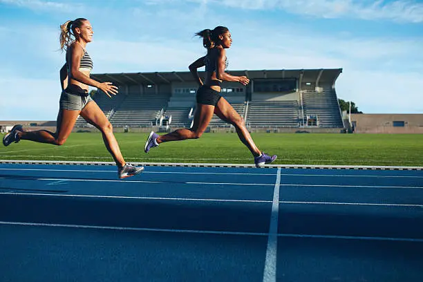 Athletes arrives at finish line on racetrack during training session. Young females competing in a track event. Running race practicing in athletics stadium.