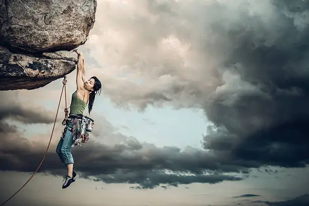 Female climber dangles from the edge of a challenging cliff.