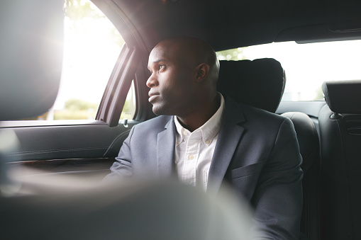 Young african businessman traveling to work in the luxury car on the back seat looking outside the window.