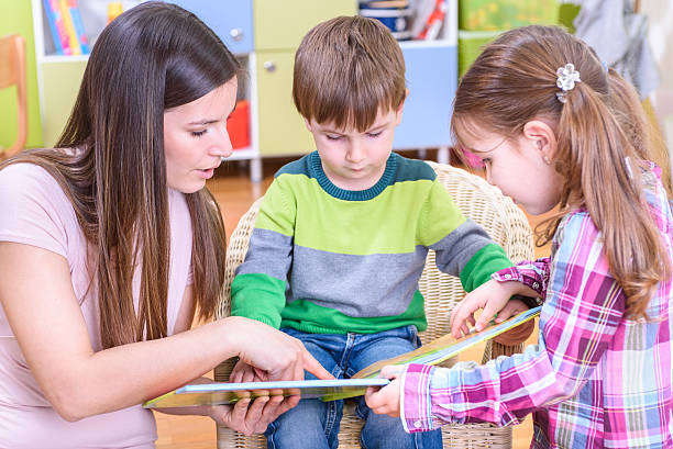 istock Teacher and Kids Reading a Book at Kindergarten 497480726