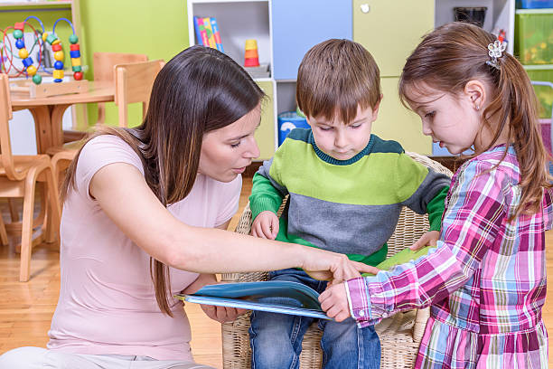 istock Teacher, Boy and Girl Reading a Book at Kindergarten 497481104