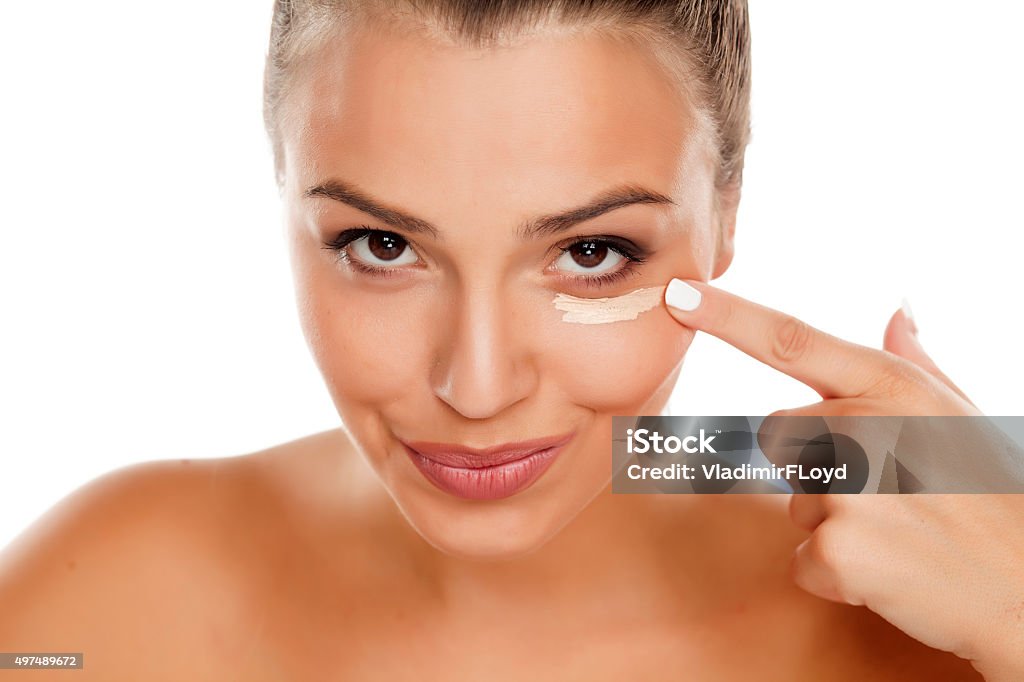 concealer Beautiful young woman applying concealer under her eyes Foundation Make-Up Stock Photo