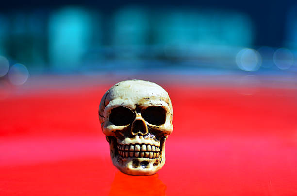 Skeleton on a red sports muscle car hood.