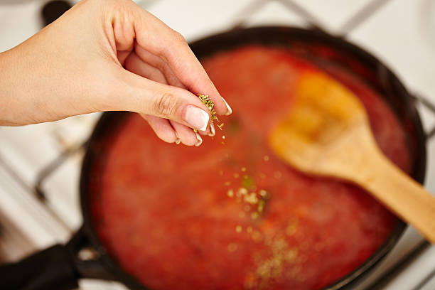 Cook's hand sprinkling parsley and basil in the sauce pan stock photo