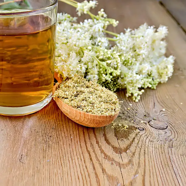 Wooden spoon with dried flowers, a bouquet of fresh flowers of meadowsweet, tea in glass mug on the wooden boards