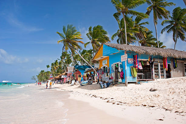 Bavaro beach in Punta Cana Punta Cana, Dominican Republic- July 20, 2013:  Tourist walking on the beach and take a tour of the bungalows-stalls with souvenirs. Locals sitting in front of stalls dominican republic stock pictures, royalty-free photos & images