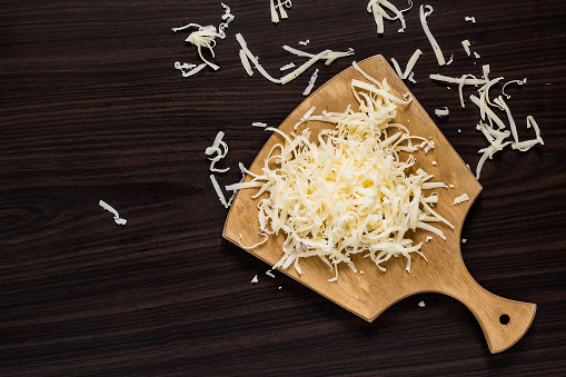 Grated cheese for cooking on a cutting board on a dark background. Top view
