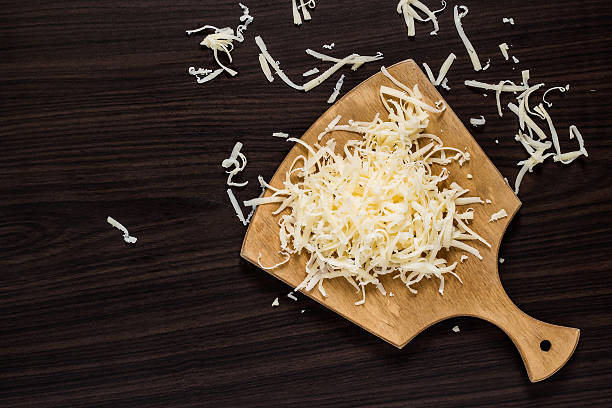 Grated cheese on a cutting board Grated cheese for cooking on a cutting board on a dark background. Top view shredded photos stock pictures, royalty-free photos & images