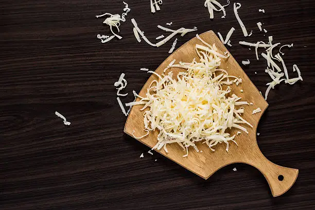 Grated cheese for cooking on a cutting board on a dark background. Top view