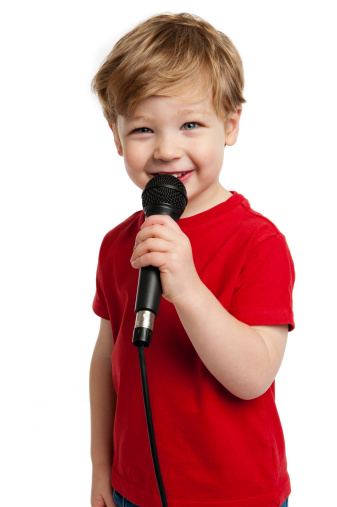 Smiling happy boy singing into a microphone shot in the studio on a white background.