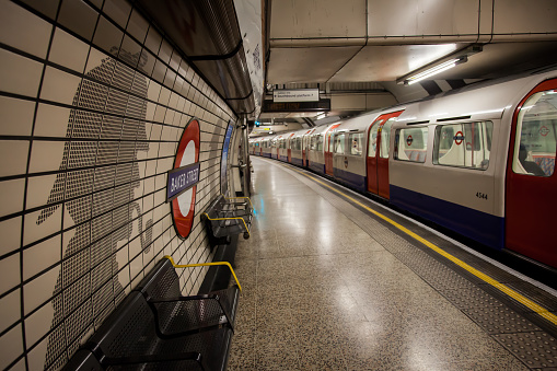 London, England - September 3, 2015: Baker Street Tube Station London with a TfL Tube Train. Passengers can be seen in the train. The platform is edged with a white line and a yellow safety line. To the left the tiled wall is decorated with a silhouette of Sherlock Holmes with benches and the London Tube Sign 