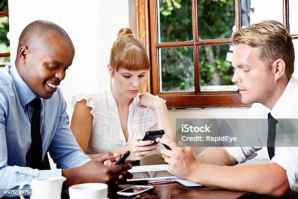 Three Young Business People In Meeting Intent On Their Cellphones Stock Photo - Download Image Now