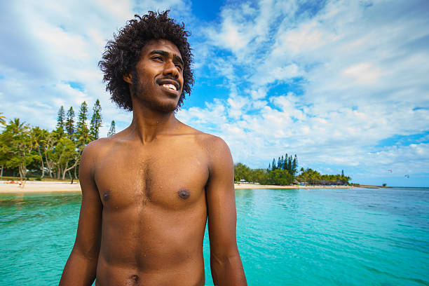 Happy smiling young pacific islander - kanak people, the original inhabitants of New Caledonia, looking over the turquoise lagoon at the beach of Noumea, New Caledonia. Real Native People Portrait. Noumea, New Caledonia, South West Pacific Ocean