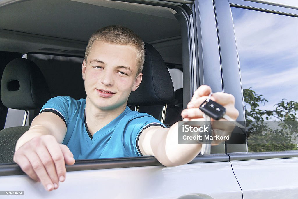 Car driver. Caucasian teen boy showing car key. Car driver. Caucasian teen boy showing car key in the new car. Happy smiling young man behind the wheel. Travel and rental concept. Close up, outdoor. 16-17 Years Stock Photo