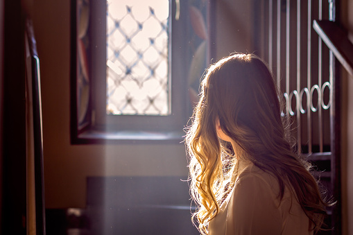 child looking out the window of the church while the light falls on her