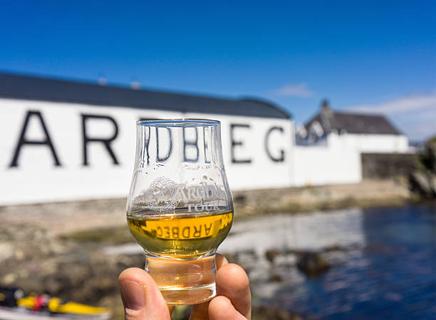 Dram of Ardbeg at the distillery on Islay Isle of Islay, UK - May 27, 2014: Close-up of a man's hands holding a taster dram of Ardbeg whisky, with a distillery building in the background. Ardbeg have produced whisky on Islay since 1798. argyll and bute stock pictures, royalty-free photos & images