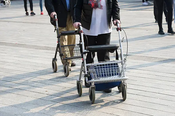 An elderly couple is walking on the street with their walking frames