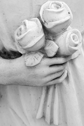 detail of cemetery  angelic sculpture with bouquet of roses in hand