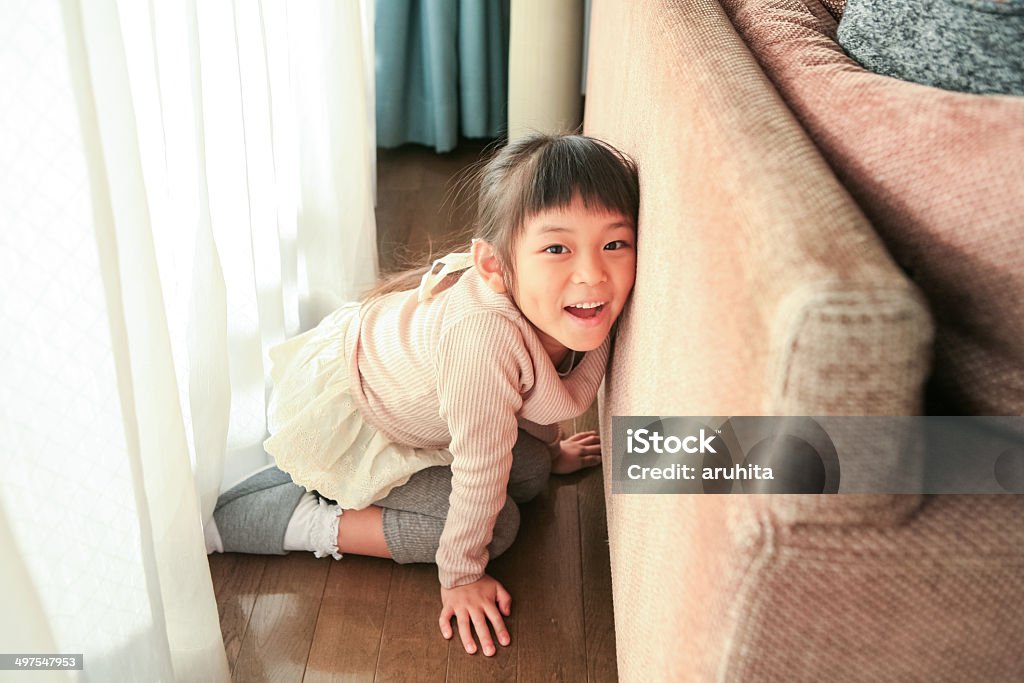 Girl hiding behind the sofa A girl is hiding behind the sofa and waiting for grandparents to find her out. Hide And Seek Stock Photo